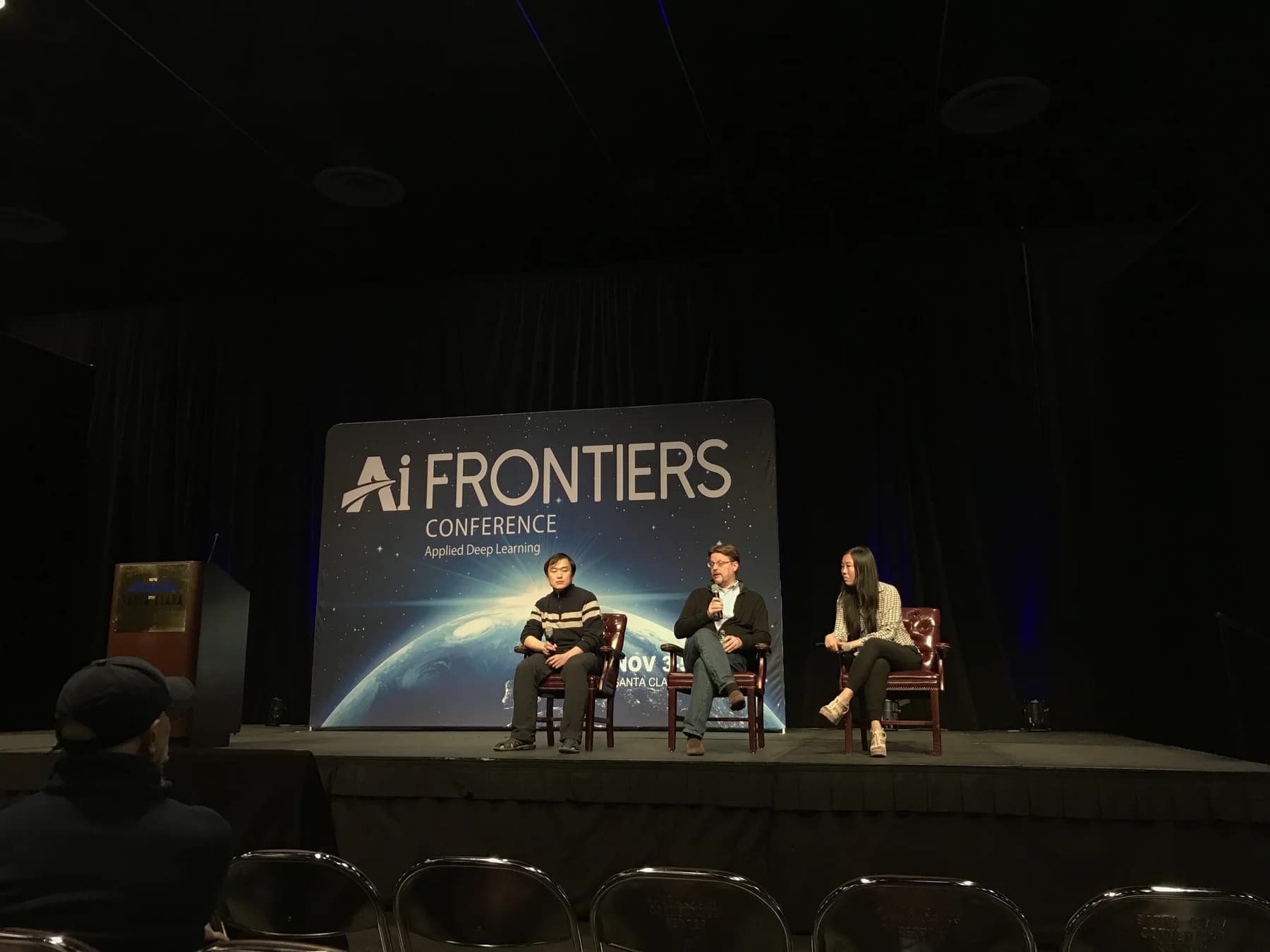 A panel discussion on the AI Frontiers 2017 stage with three speakers seated in front of the event backdrop.