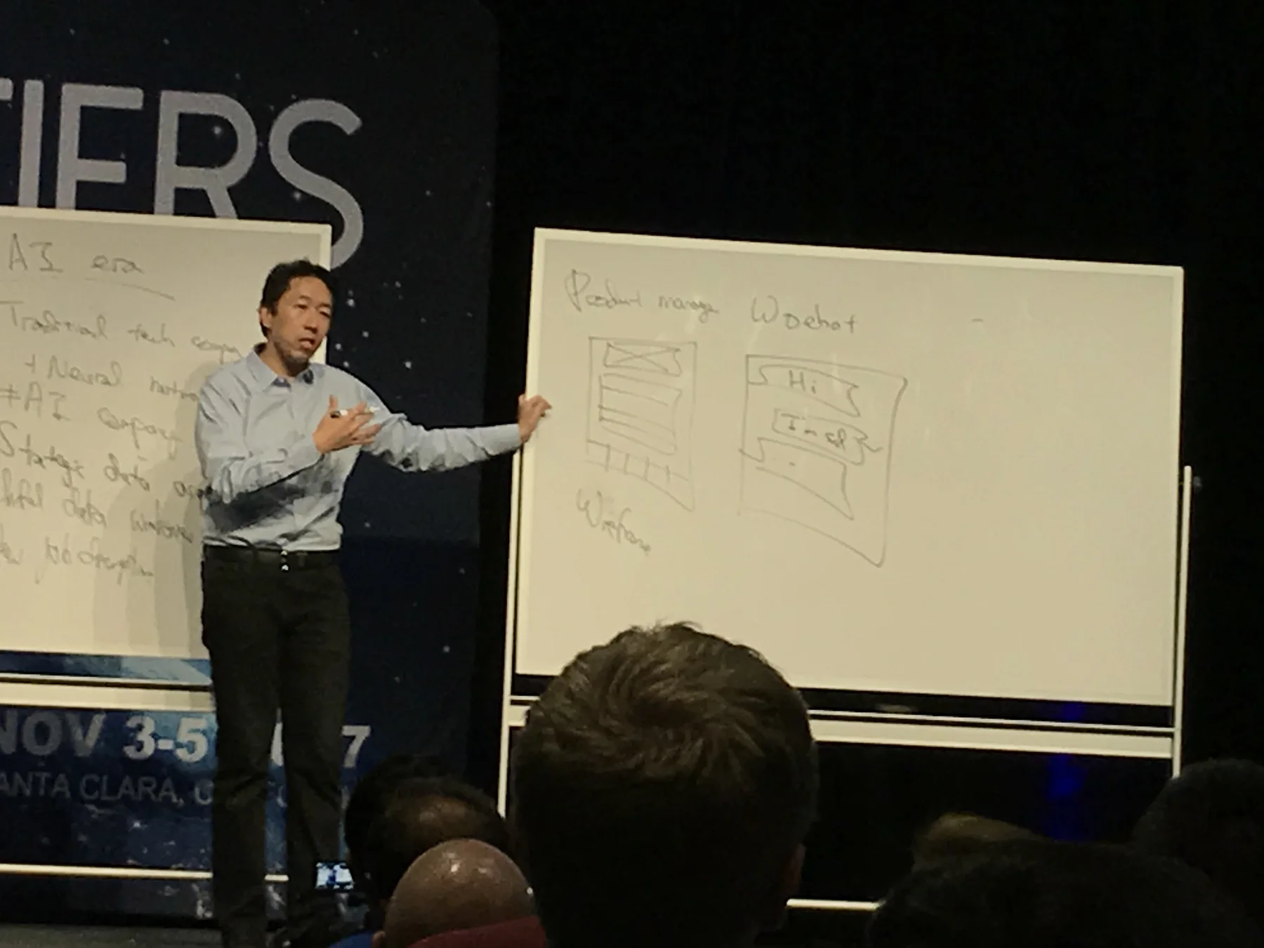 A speaker at AI Frontiers 2017 standing beside whiteboards with product manager and chatbot sketches.