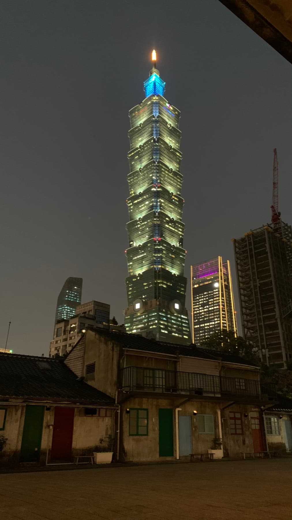 Taipei 101 illuminated at night behind low historic buildings.