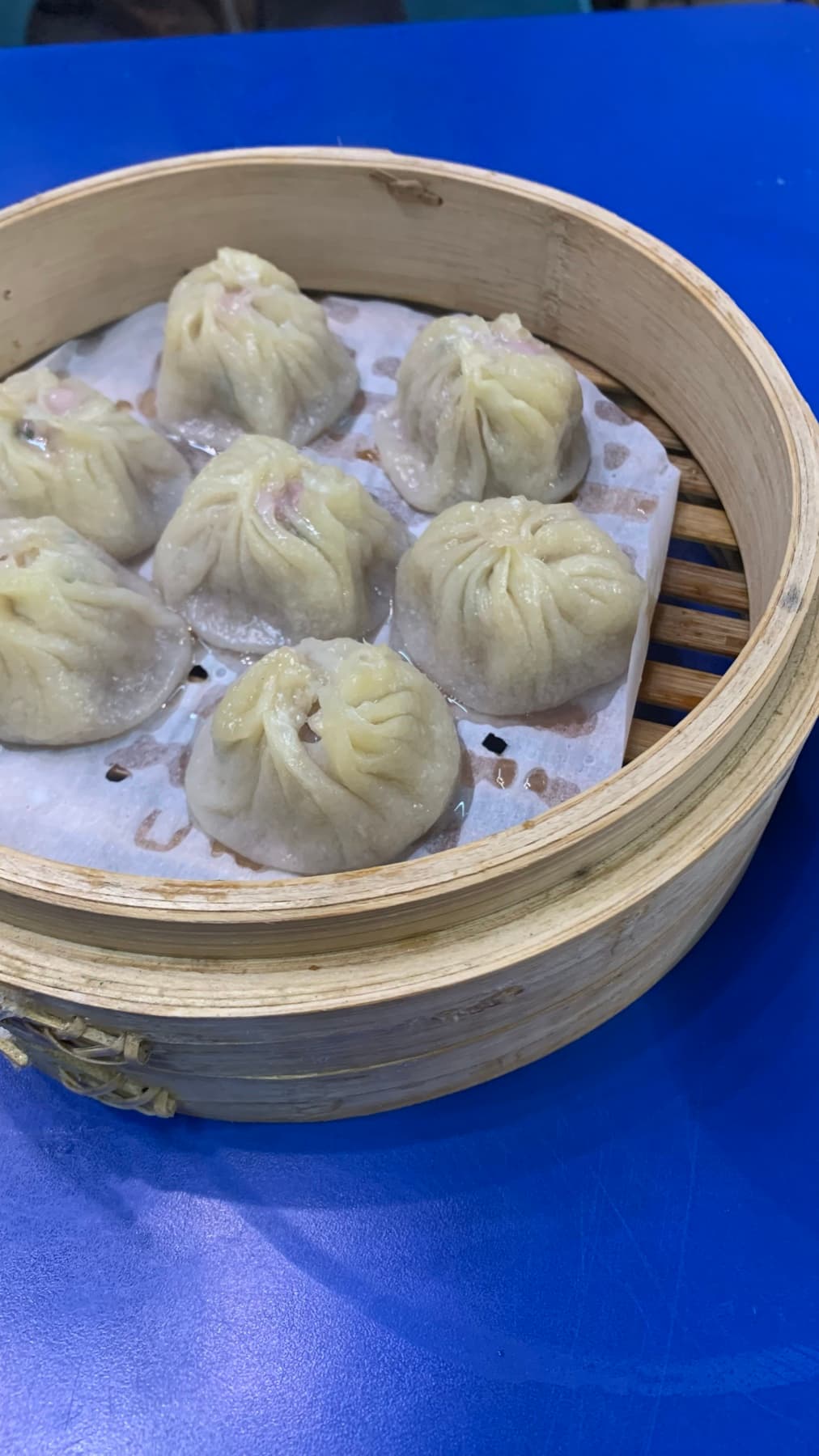 A bamboo steamer basket of xiao long bao on a blue table in Taipei.
